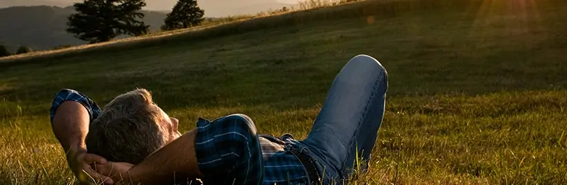 Man laying on grass with hands behind his head to demonstrate the positive and peaceful feeling someone with PTSD can experience once they cure their PTSD or PTSI